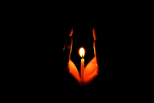 Hände beschützen eine Kerzenflamme